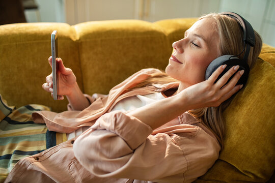 Woman relaxing on sofa listening to music on smartphone