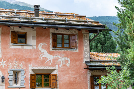 A white ibex and lobster sgraffito decorating the salmon-pink facade of a traditional Engadine house in S-Chanf with wooden shutters in Switzerland