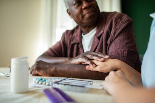 Senior man holds caregiver?s hand at home with medication