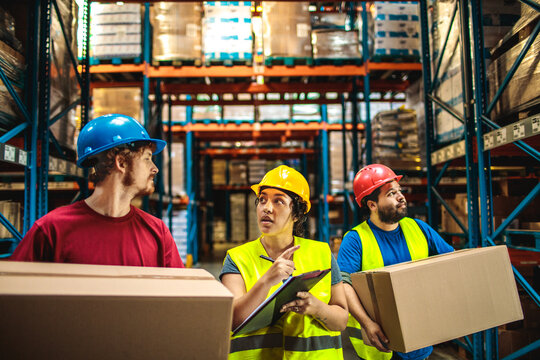 Warehouse workers carrying boxes while supervisor gives instructions