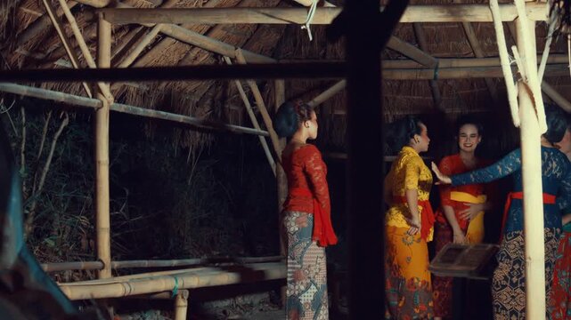 Side profile view of a line of female dancers in colorful Kebayas standing one behind another, possibly preparing for a formation.