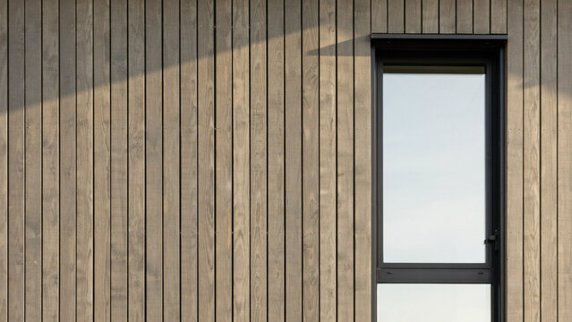 Dark stained vertical wooden wall cladding with single black frame rectangular home window.