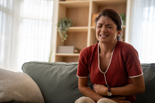Stress, stomach pain and woman on a sofa with menstruation, gas or constipation, pms or nausea at home. Gut health, anxiety and lady with tummy ache in living room from ibs, bloated or endometriosis