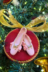 Delicate pink ballet slippers displayed on red circular base with golden ribbon amidst Christmas tree foliage, elegant holiday display, festive atmosphere theater arts.  © Алла Чеснокова