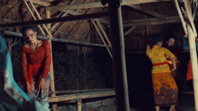 Cinematic footage of a solitary woman in a red traditional dress looking downcast in the foreground, while her friends dance happily in background.