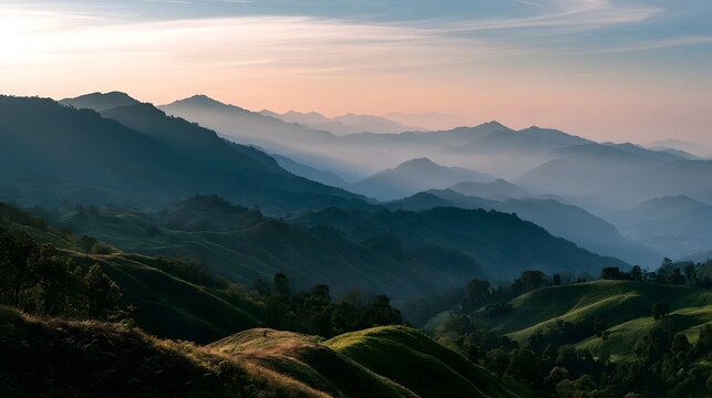 Rolling green hills and layered mountain ranges under a soft pastel sky at sunrise or sunset