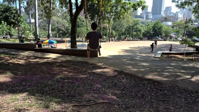 A 13 year old Brazilian teenager sitting on a swing in a public square.