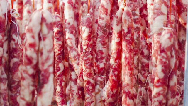 Raw marbled sausages hanging in a row at a butchery display