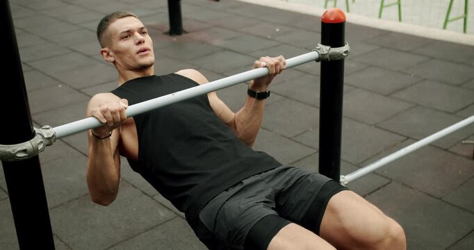 Young athletic man exercising outdoors and pull up on horizontal bar. Fitness and sport lifestyle. Sports, health care. Sporty guy has workout and training arms and core muscles at sport ground.