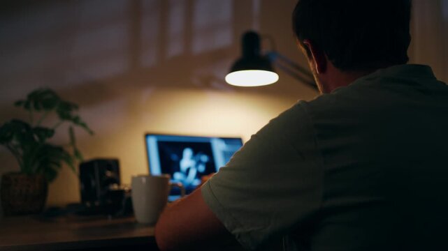 Tired man working late on laptop at home, hold head in frustration and exhaustion, illustrating work stress, professional pressure, creative block and the challenges of remote work