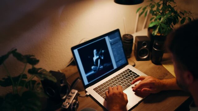 Professional photographer or digital artist working on a laptop, retouching a black and white fashion photograph in a creative studio office workspace at night