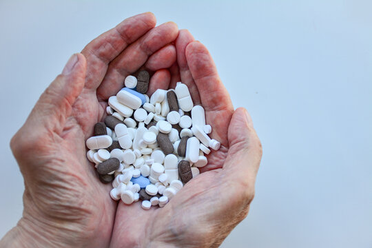Older hands hold a large assortment of tablets and pills against a pale background. Close-up healthcare concept useful for pharmacy, medication, treatment and senior care
