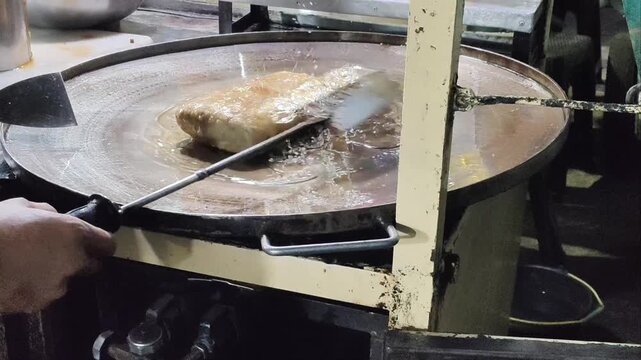A street food vendor cooks Martabak Telur, a traditional Indonesian stuffed pancake, on a hot flat pan filled with oil at a local night market