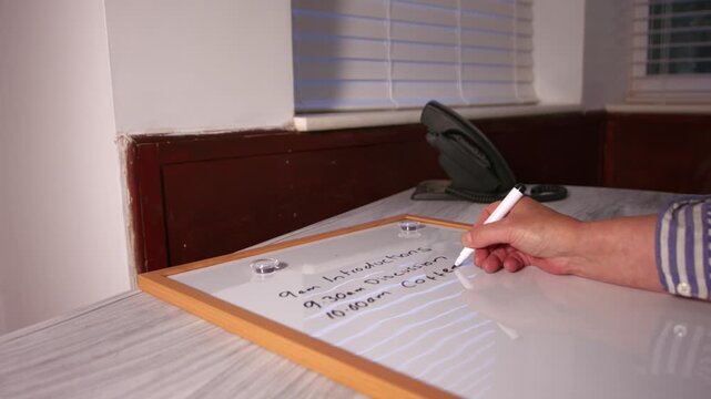Hand writing out meeting schedule on whiteboard