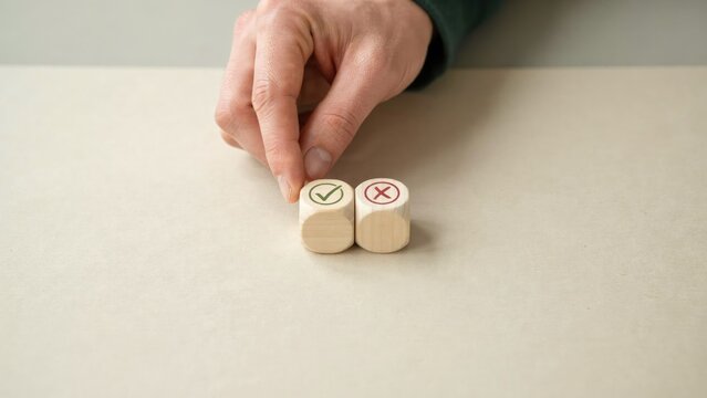Hand placing a wooden cube with a green checkmark next to a cube with a red cross on a beige surface