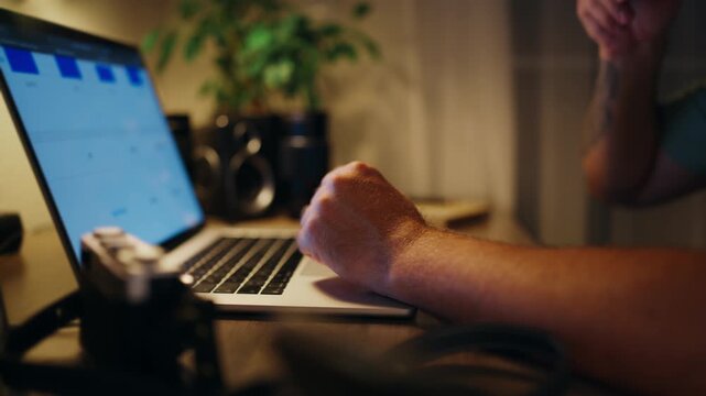 Close-up of a determined man working late into the night on his laptop, taking a sip of coffee to stay energized while continuing to type and focus on his project
