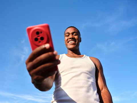 Smiling man taking selfie with smartphone against blue sky