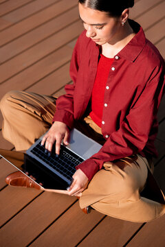 Woman using laptop while seated on sunlit wooden terrace