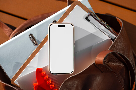 Phone mockup with white screen among office documents and bag