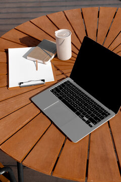 Person laptop, clipboard and coffee arranged on sunny wooden terrace