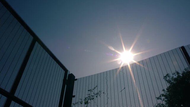Intimidating high metal fence with bright sun background
