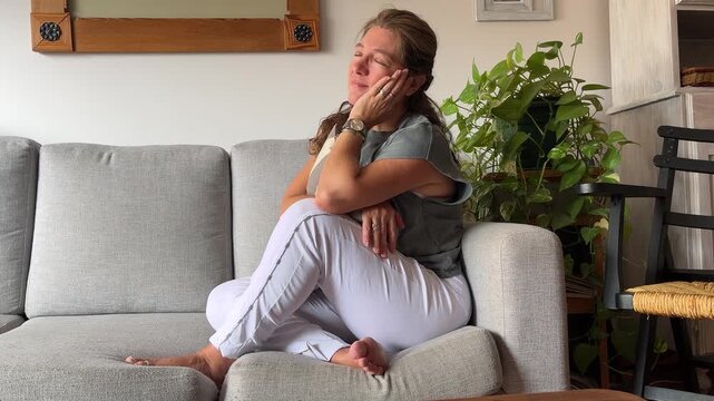 Peaceful mid adult woman relaxing on a cozy sofa at home enjoying a moment of serenity and calm mindfulness