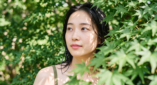 Portrait of a young woman gently framed by vibrant green leaves and foliage in soft natural light. Fresh, organic beauty and nature concept.