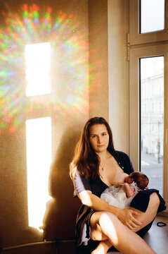 Mother Breastfeeding Baby by the Window With Sunlight in Room