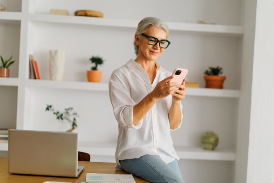 Senior woman smiling using smartphone at home office