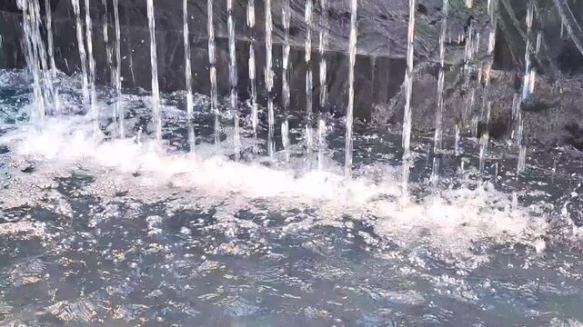 artificial waterfall streams cascading down dark stone wall into splashing pool water surface modern garden architectural fountain feature