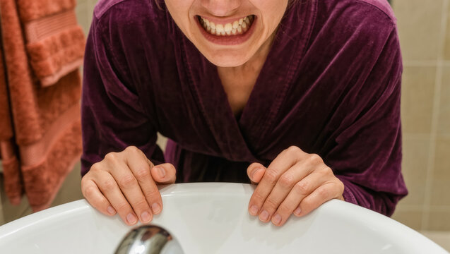 Person in purple bathrobe baring teeth at bathroom sink