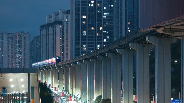 Elevated Monorail Train Passing High-Rise Apartment Buildings at Night in Urban City