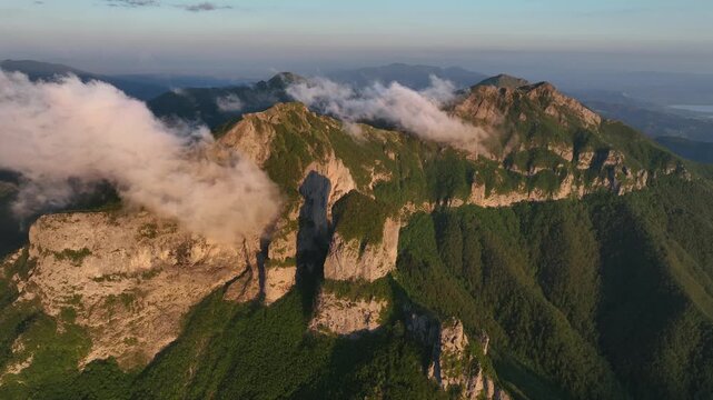 Aerial view of the rugged peaks and rocky cliffs of Foce del Pallone with wispy clouds clinging to the mountainside in Stazzema, Toscana, Italy.