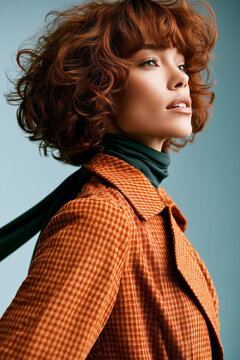 Stylish woman with curly red hair looking away while posing in an autumn orange houndstooth coat and dark turtleneck.