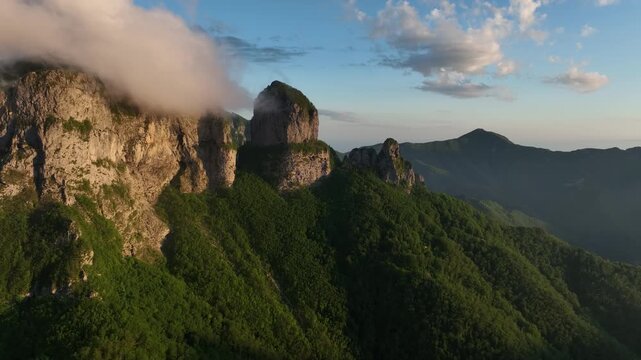Aerial view of the rocky Foce del Pallone mountain peaks surrounded by clouds and lush green slopes at sunset in Stazzema, Toscana, Italy.