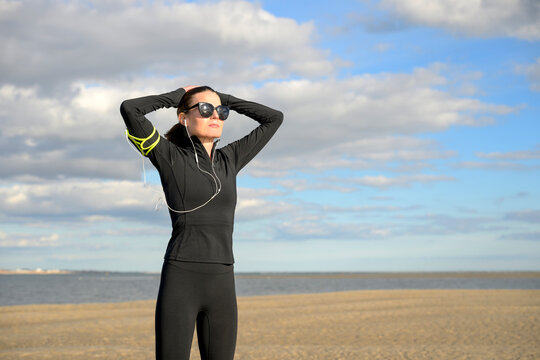Woman in Sportswear Stretching on a Beach, Hands on Head