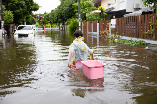 Back view, Asian boy wearing Raincoat walking through floodwaters, lifestyle of Thai people in massive flooding, Severe weather