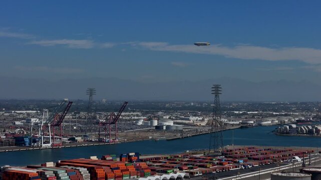Aerial view of the Port of Long Beach with shipping containers, industrial cranes, and an airship flying in the sky over Long Beach, California, United States.
