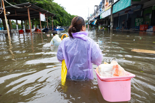 Back view, obese woman wearing Raincoat and walking through flood waters to go buy food, lifestyle of Thai people in massive flooding, Severe weather