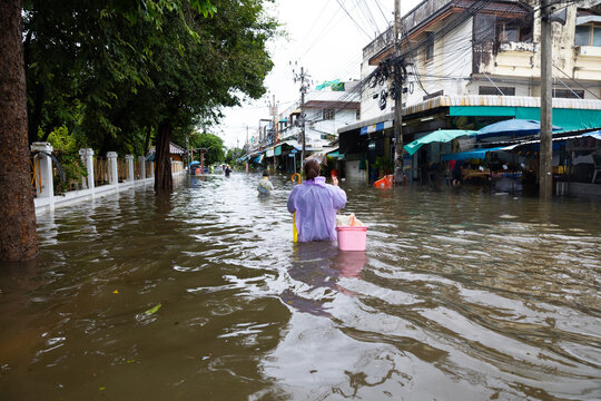 Back view, obese woman wearing Raincoat and walking through flood waters to go buy food, lifestyle of Thai people in massive flooding, Severe weather