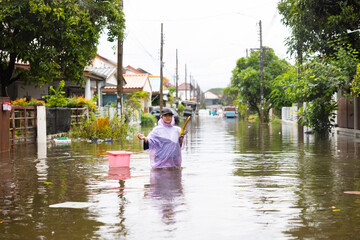 Fototapeta premium obese woman wearing Raincoat and walking through flood waters to go buy food, lifestyle of Thai people in massive flooding, Severe weather