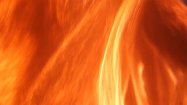 Orange flames of a fire, filmed in close-up, rise upwards, swirling and shimmering