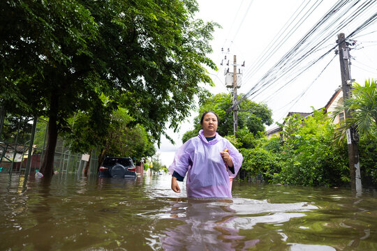obese woman wearing Raincoat and walking through flood waters to go buy food, lifestyle of Thai people in massive flooding, Severe weather