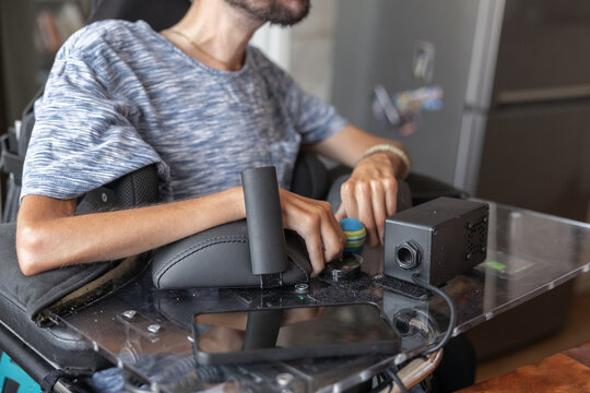 A man uses assistive technology to control his wheelchair in his living area. He engages with the equipment for independent living.