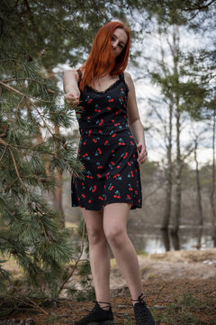 Red-haired woman stands beneath pine tree branches