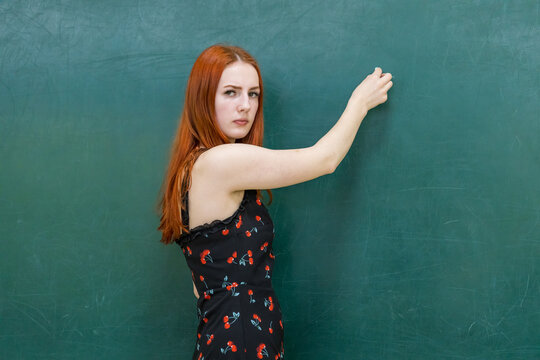 Red-haired woman stands before a green chalkboard