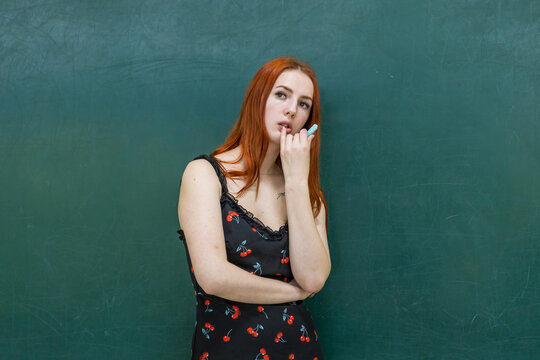 Red-haired woman stands pensively against a green chalkboard