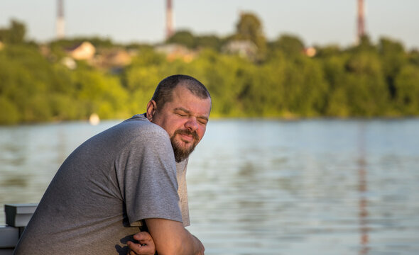 Man sits by calm lake, eyes closed, relaxed