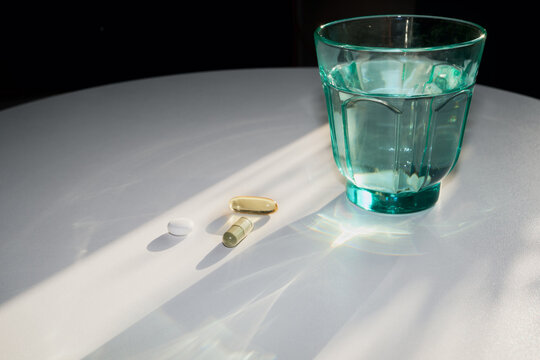 Pills and capsules on table next to glass of water for daily wellness