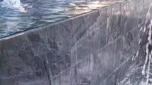 Clear Water Overflowing Over Modern Dark Granite Fountain Wall Edge In Outdoor Architecture Feature
